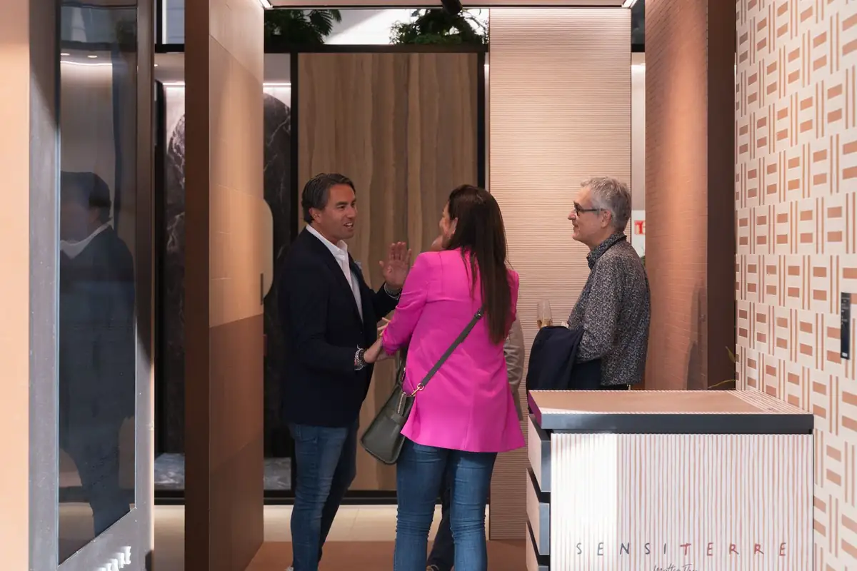 Three guests talking next to a unit bearing the SensiTerre sign and a wall with a geometric pattern