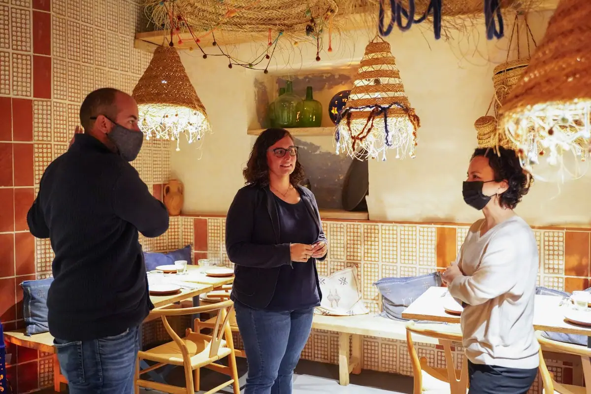 Tres personas conversan en un comedor de Blau by Foodies con paredes de piezas cerámicas y lámparas de fibra natural