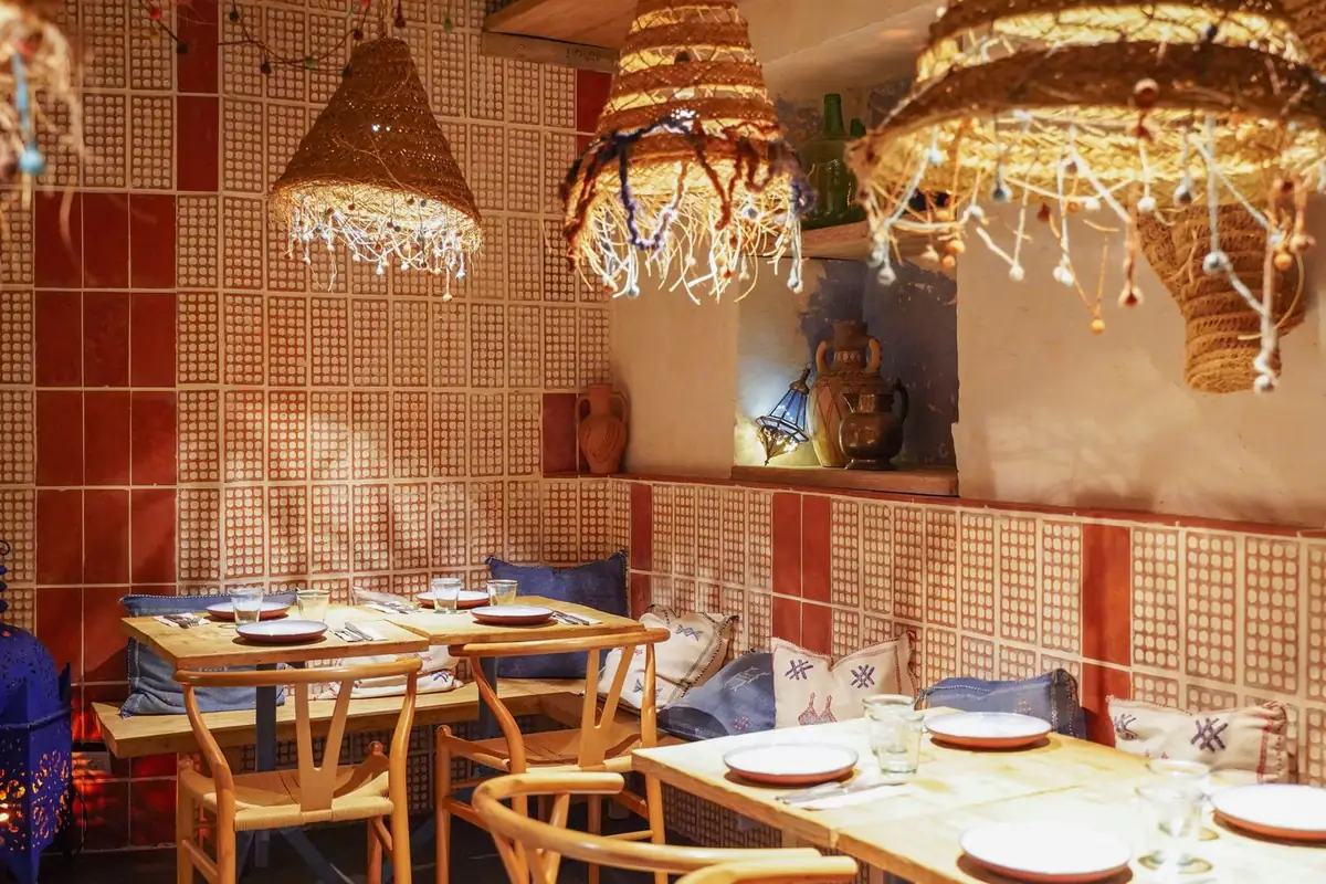 Comedor de Blau by Foodies con paredes de piezas cerámicas perforadas y rojas, mesas de madera y lámparas de fibra natural