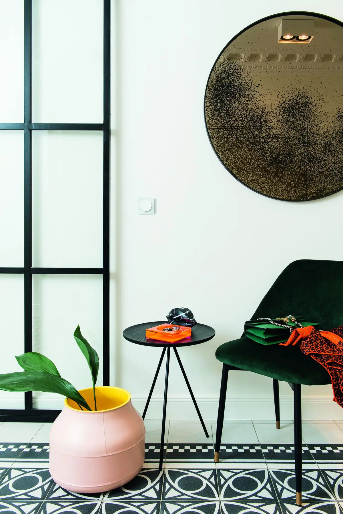 Hallway with a white switch on the wall, a round mirror, a black side table and a green velvet chair