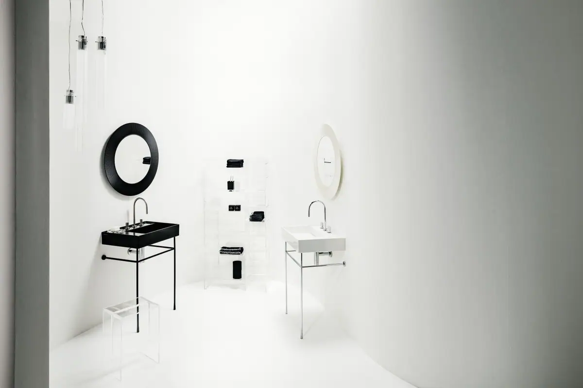 Two washbasins, one black and one white, on metal frames, with round mirrors, transparent shelving and pendant lamps
