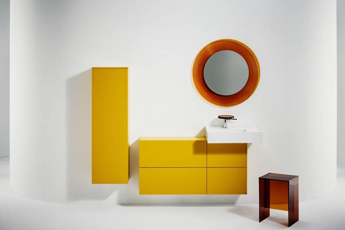 Yellow tall cabinet and vanity units with a white washbasin, a round orange mirror and an amber transparent stool