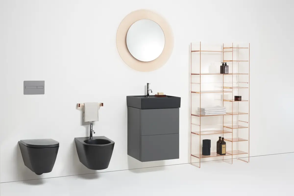 Dark wall-hung WC and bidet, a grey vanity unit, a round pink mirror and copper transparent shelving