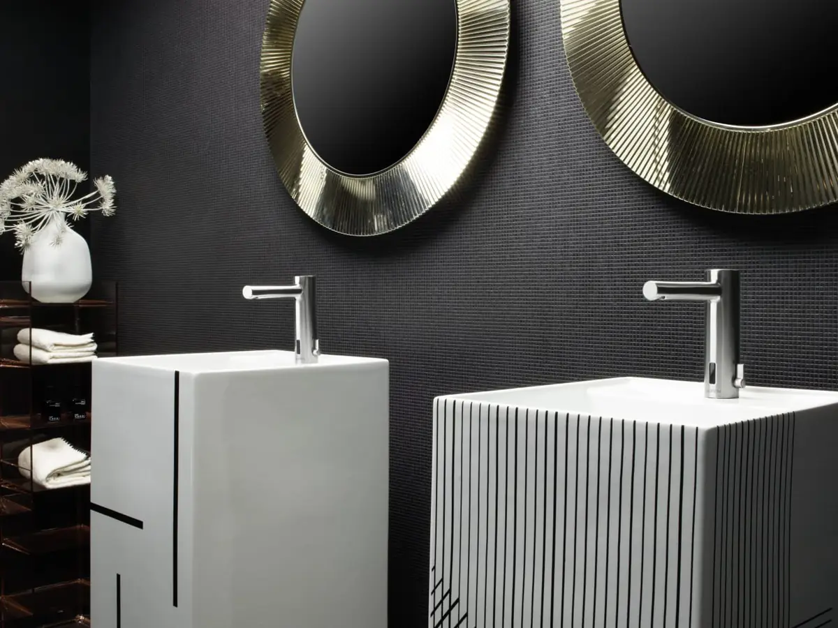 Two white freestanding washbasins with black line decorations under two round gold mirrors
