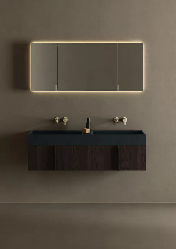 Wall-hung Paral unit in dark oak with a black double washbasin, wall-mounted gold taps and a backlit mirror cabinet.