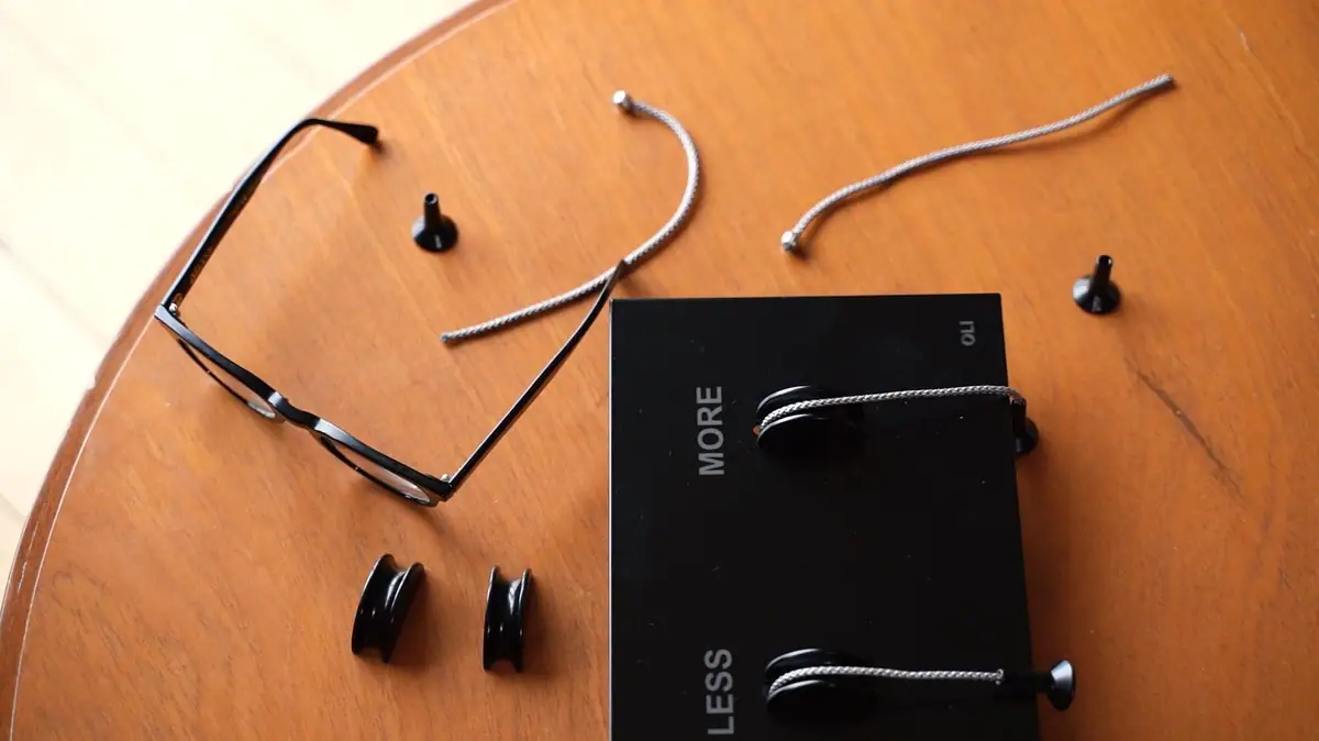 Black LESS is MORE plate on a wooden table next to grey braided cords, pulls, pulleys and a pair of glasses