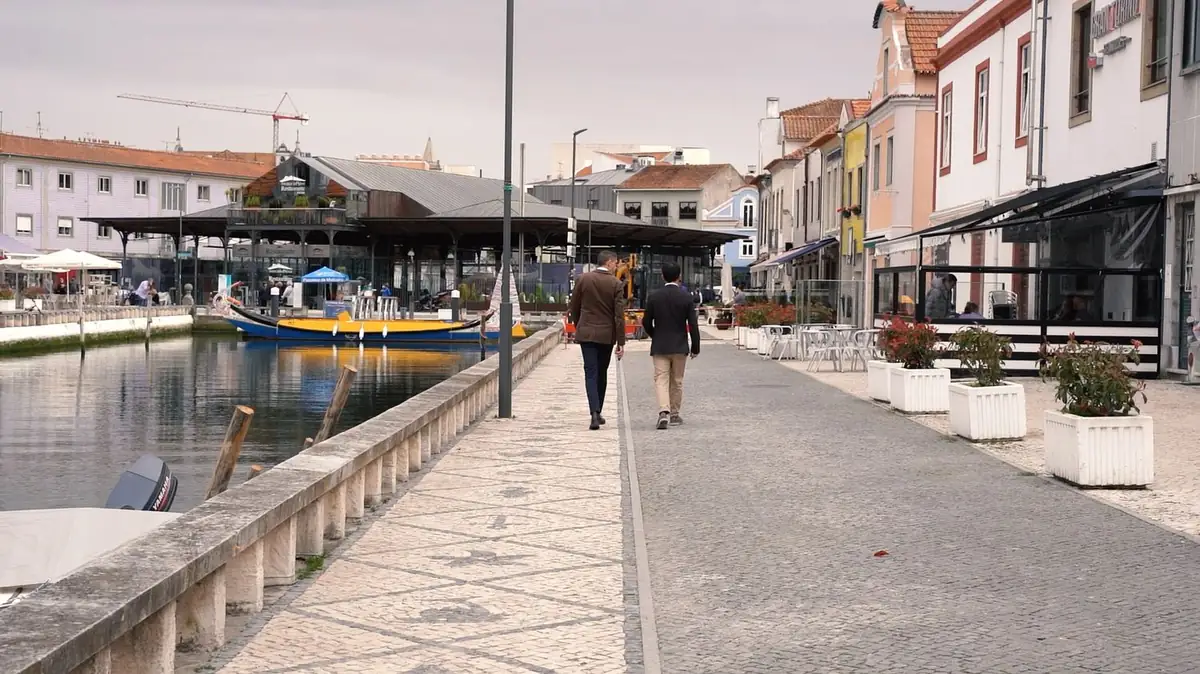 Two men walk along a promenade beside a canal with a yellow and blue boat and colourful façades