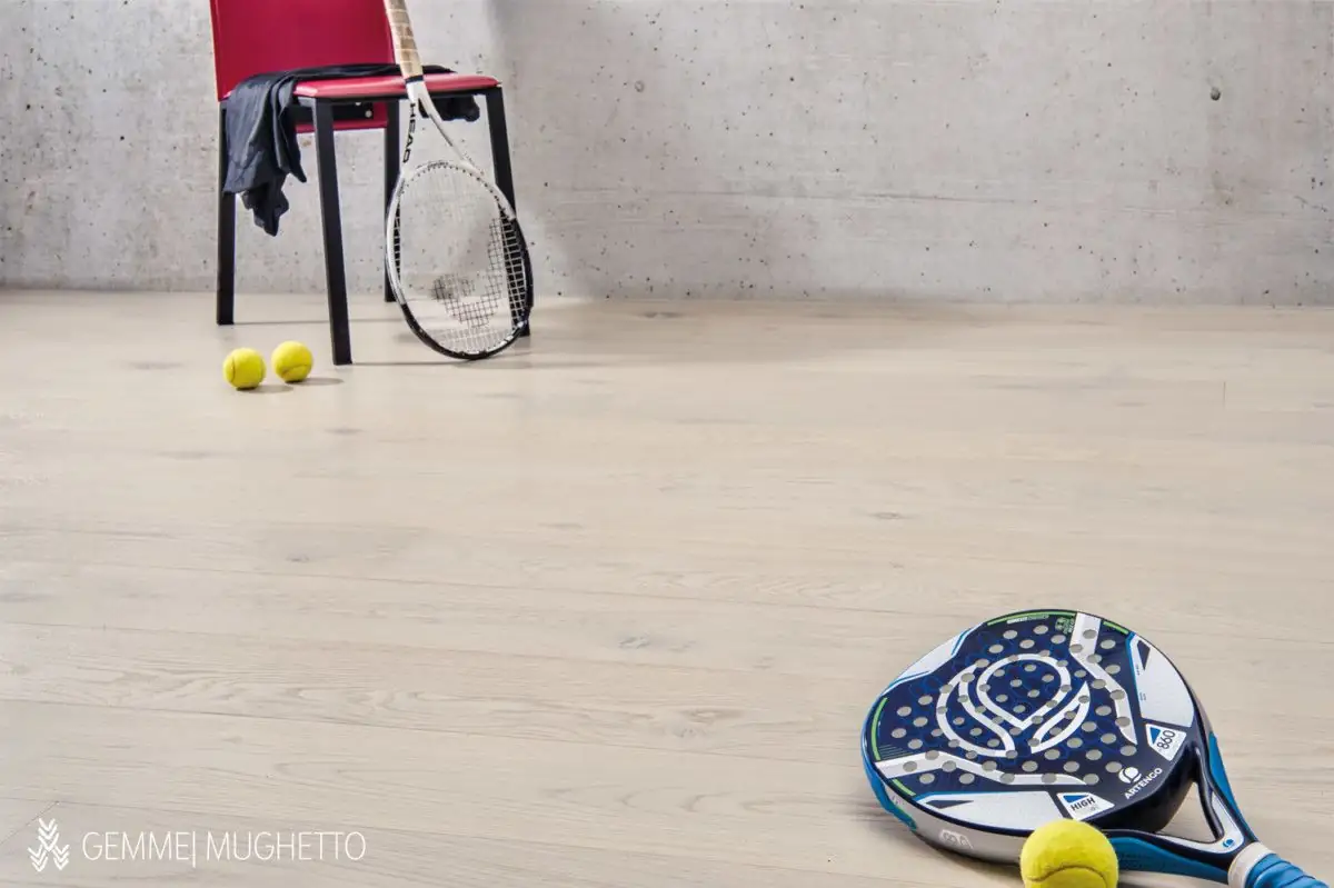 Floor of very light oak boards with a red chair, a tennis racket, balls and a padel racket