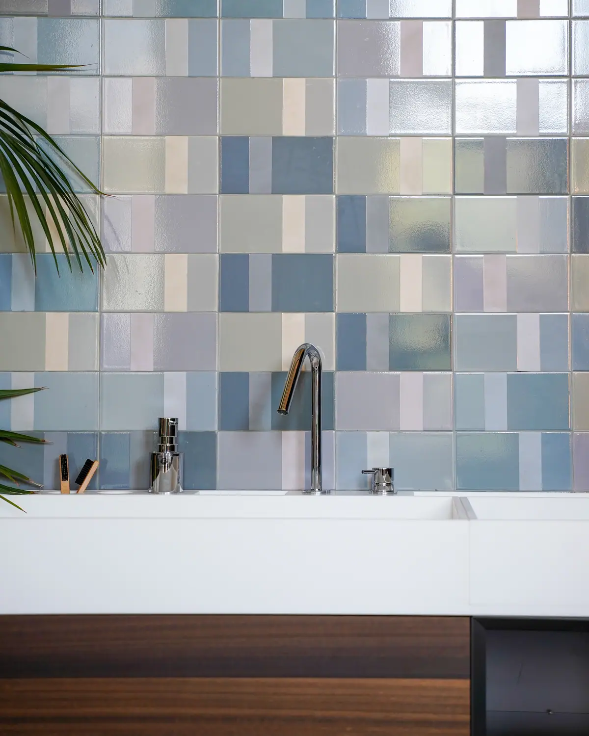 White basin with a tall chrome spout and separate control, in front of a wall of tiles in blue and grey tones.