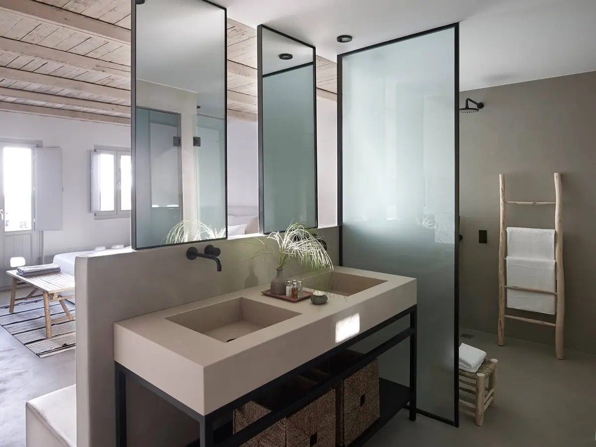 Hotel bathroom with a double built-in basin in a sand tone, black wall-mounted taps and a translucent glass screen.