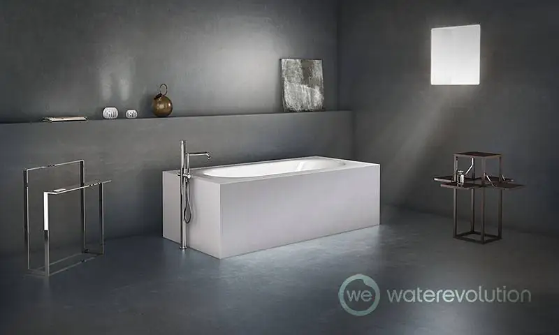 White bath with a chrome floor-standing bath tap, metal towel rail and side table in a bathroom with grey walls.