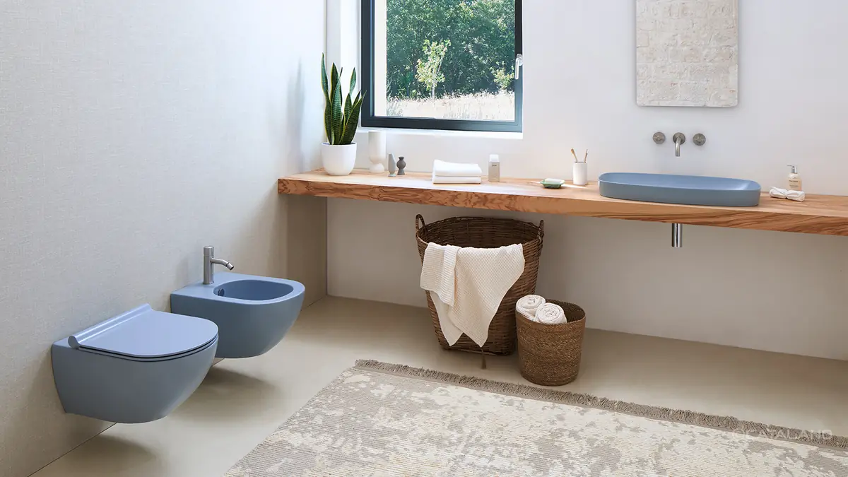 Bathroom with a satin blue washbasin on a wooden worktop beneath the window and a wall-hung WC and bidet in the same colour