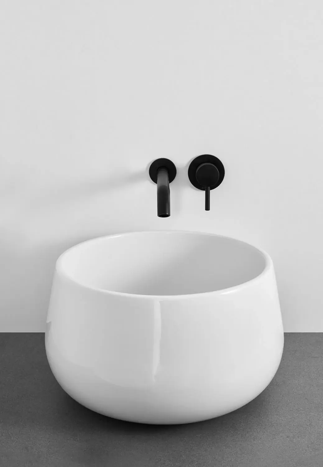 Lavabo de apoyo redondo blanco brillante, alto y de paredes abombadas, con grifería mural negra
