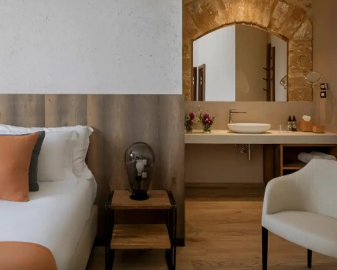 Hotel bedroom with an open washbasin area, a white countertop washbasin on a light worktop and a mirror framed by a stone arch