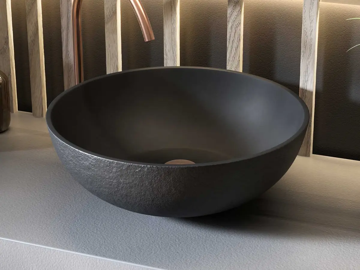 Dark round countertop washbasin with a textured exterior, on a grey worktop with a tall copper spout tap