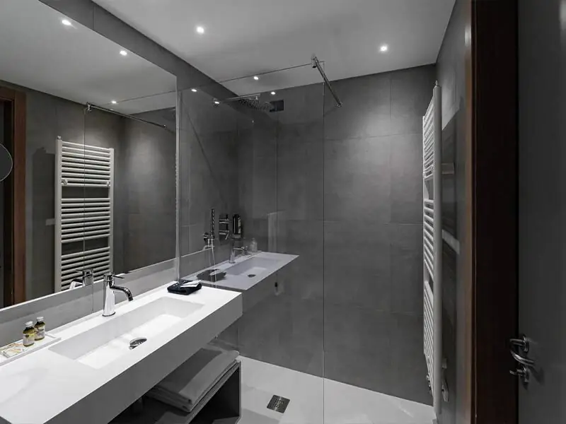 Hotel bathroom with a long white worktop with integrated washbasin opposite a walk-in shower, with grey walls and a white towel rail