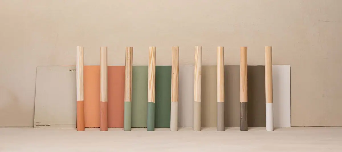 Wooden rods with ends painted in terracotta, green, sand, grey and white resting on paint samples of the same colours