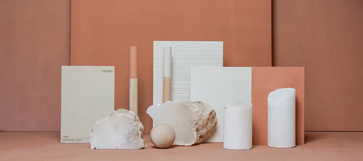 Composition of lime stucco samples in white and terracotta with stones, cylinders and a wooden sphere on a terracotta background