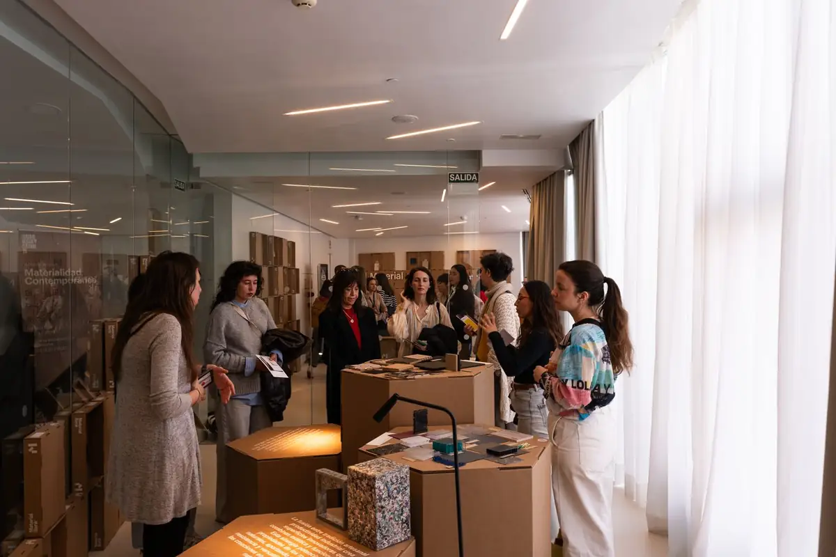 Grupos de visitantes recorren la sala entre peanas con muestras, junto a una pared de vidrio