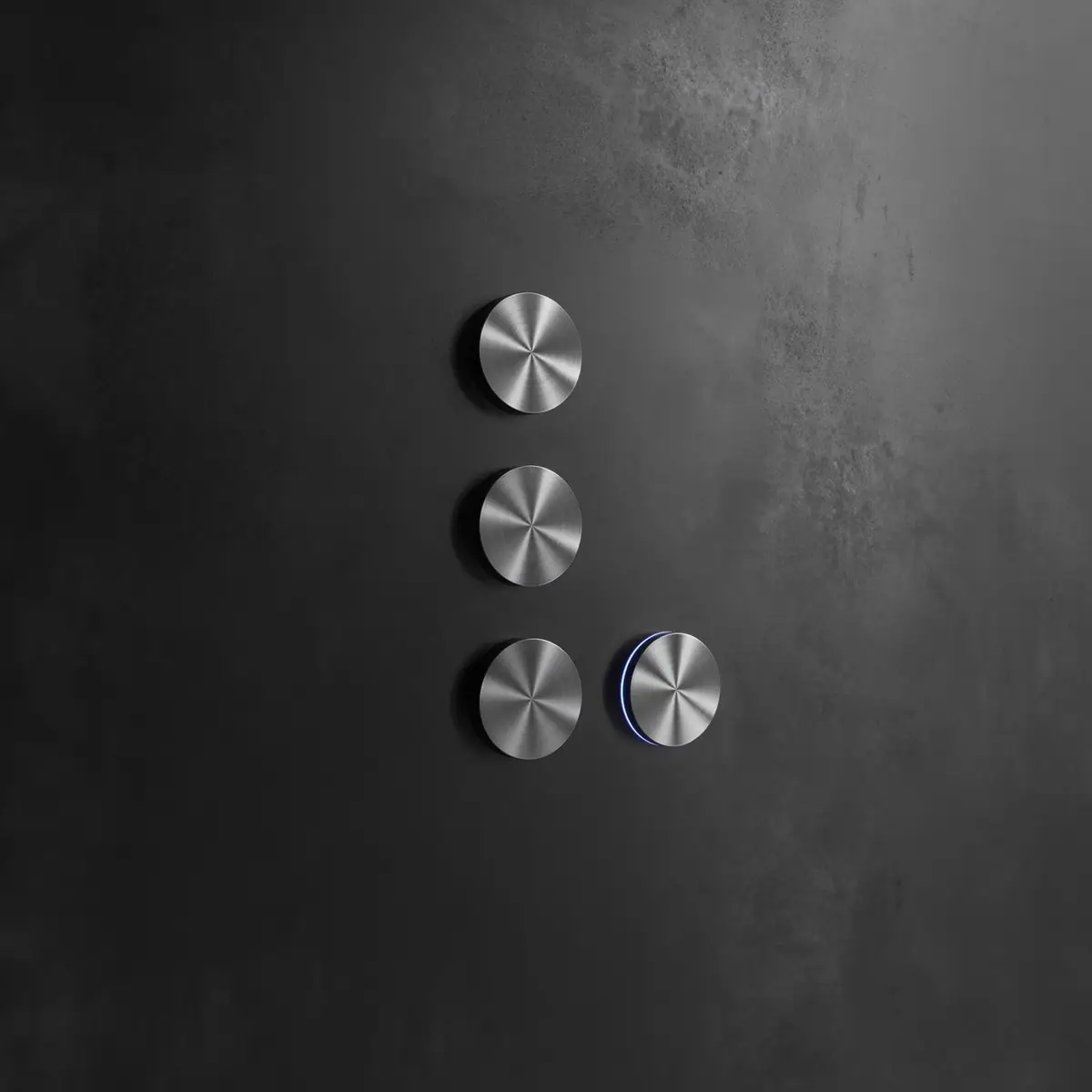 Four circular stainless steel controls on a dark wall, one with a blue light ring