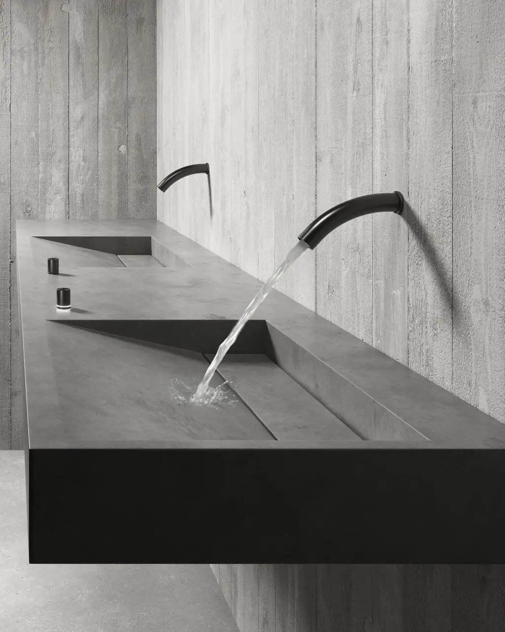 Long concrete basin with two black wall-mounted spouts and small controls on the worktop