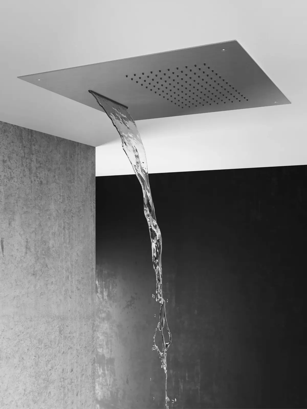 Steel ceiling shower head releasing a sheet of water next to a concrete wall
