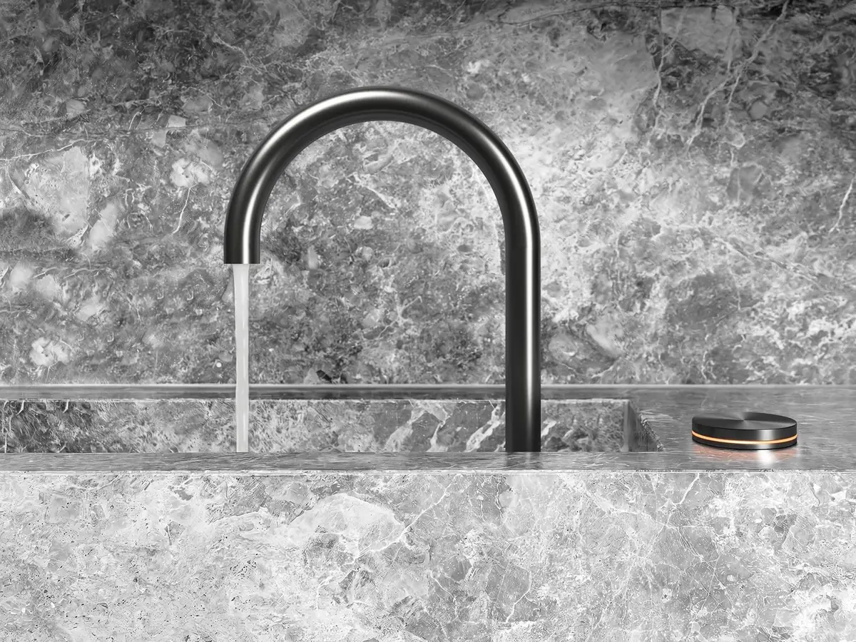 Dark kitchen tap with a curved spout over a grey marble sink, with a circular control beside it