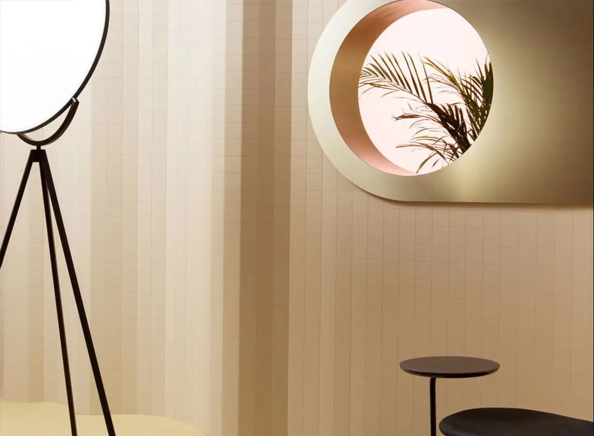 Wall clad in a mesh of cream-toned rectangular pieces forming vertical folds, next to a floor lamp and a round mirror.