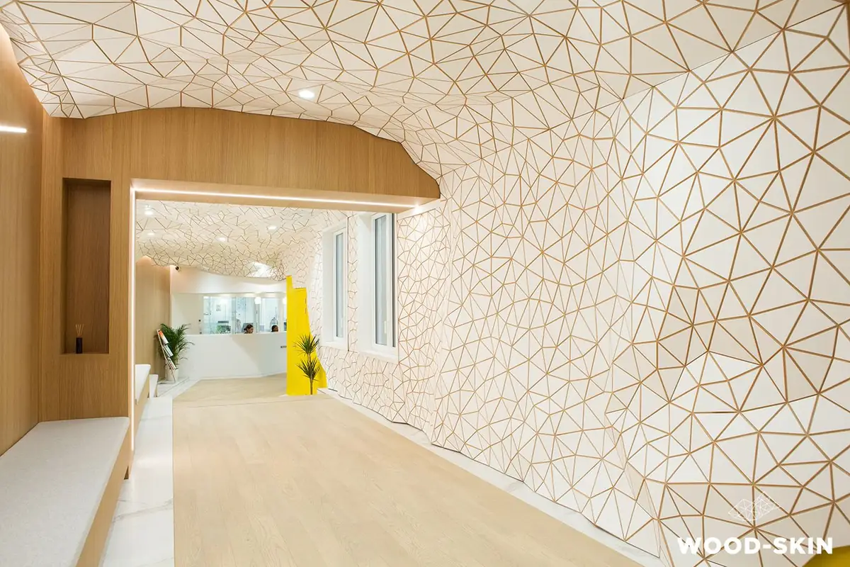 Corridor with a wall and ceiling covered in a white tessellated mesh that runs up to a yellow wall, with a light wood floor.