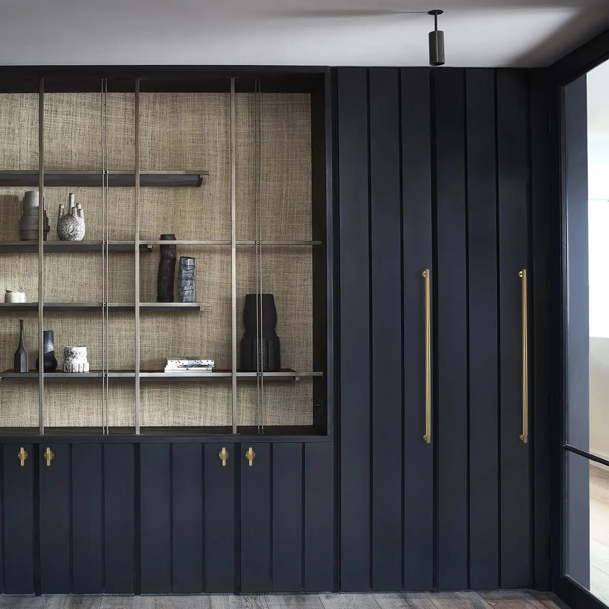 Wardrobe with dark blue lacquered fronts, long brass pull handles and metal shelving with a natural-fibre back