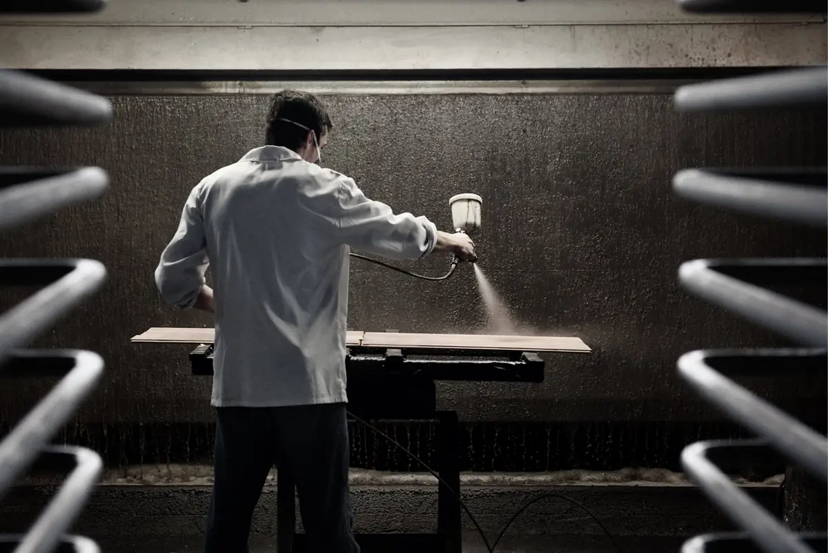 Worker spraying colour onto a wooden board in a spray booth.