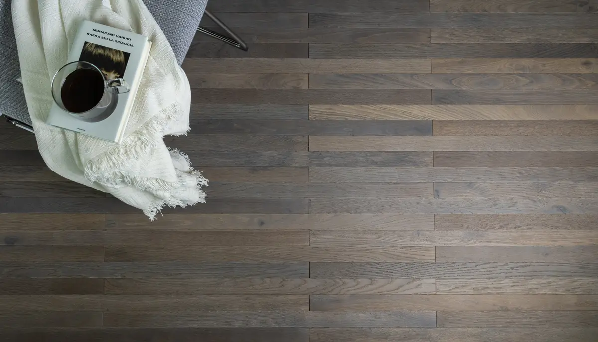 Floor of narrow oak strips in grey tones, with a throw and a book on a chair.