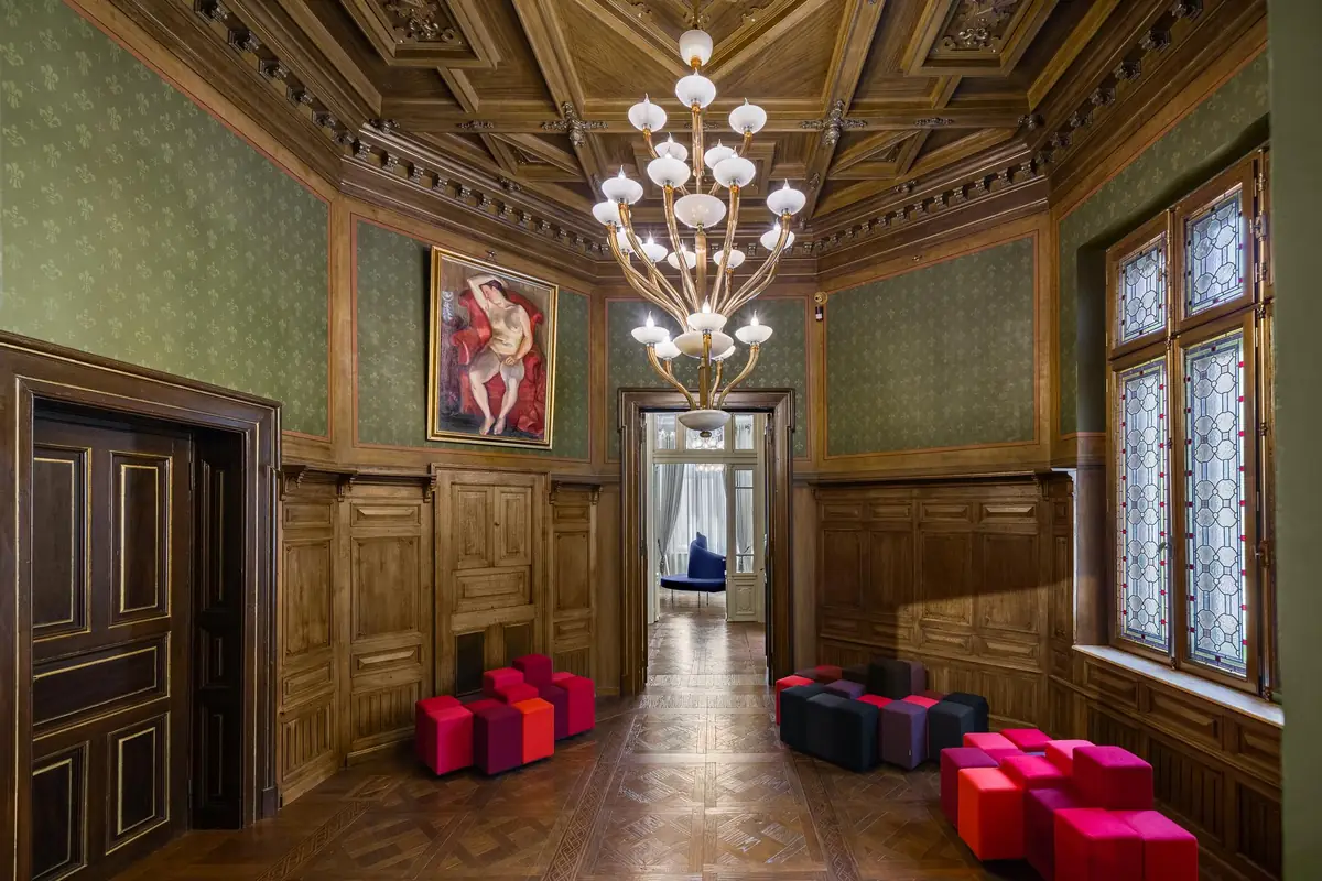 Historic room with a coffered ceiling, crystal chandelier, fabric-lined walls and dark wood floor.