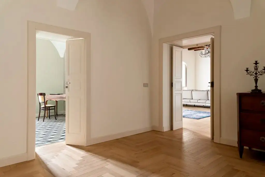 Hallway with two open doors and an oak herringbone floor continuing into the living room.