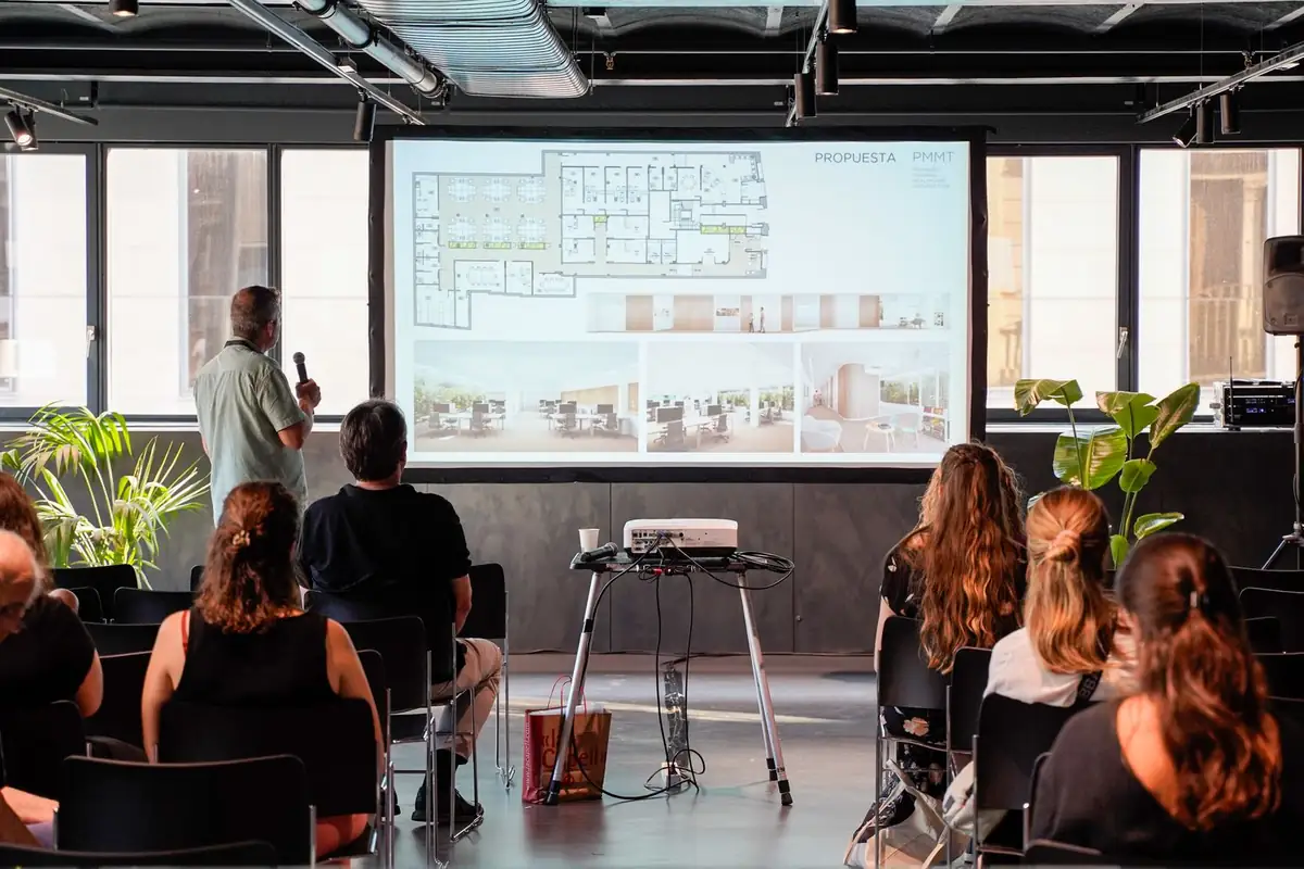 Ponente presentando plantas e imágenes de un proyecto de interiorismo ante el público.