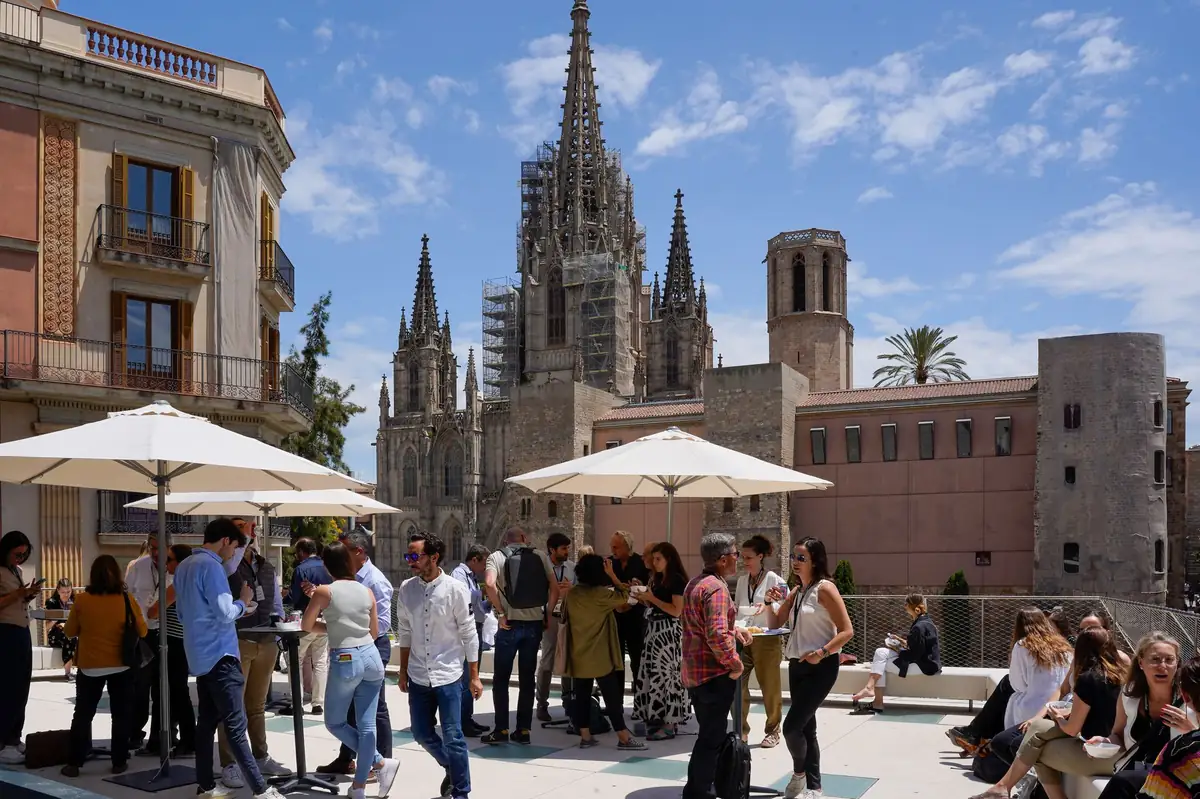 Asistentes conversando en la terraza del COAC bajo sombrillas blancas, con la catedral de Barcelona al fondo.