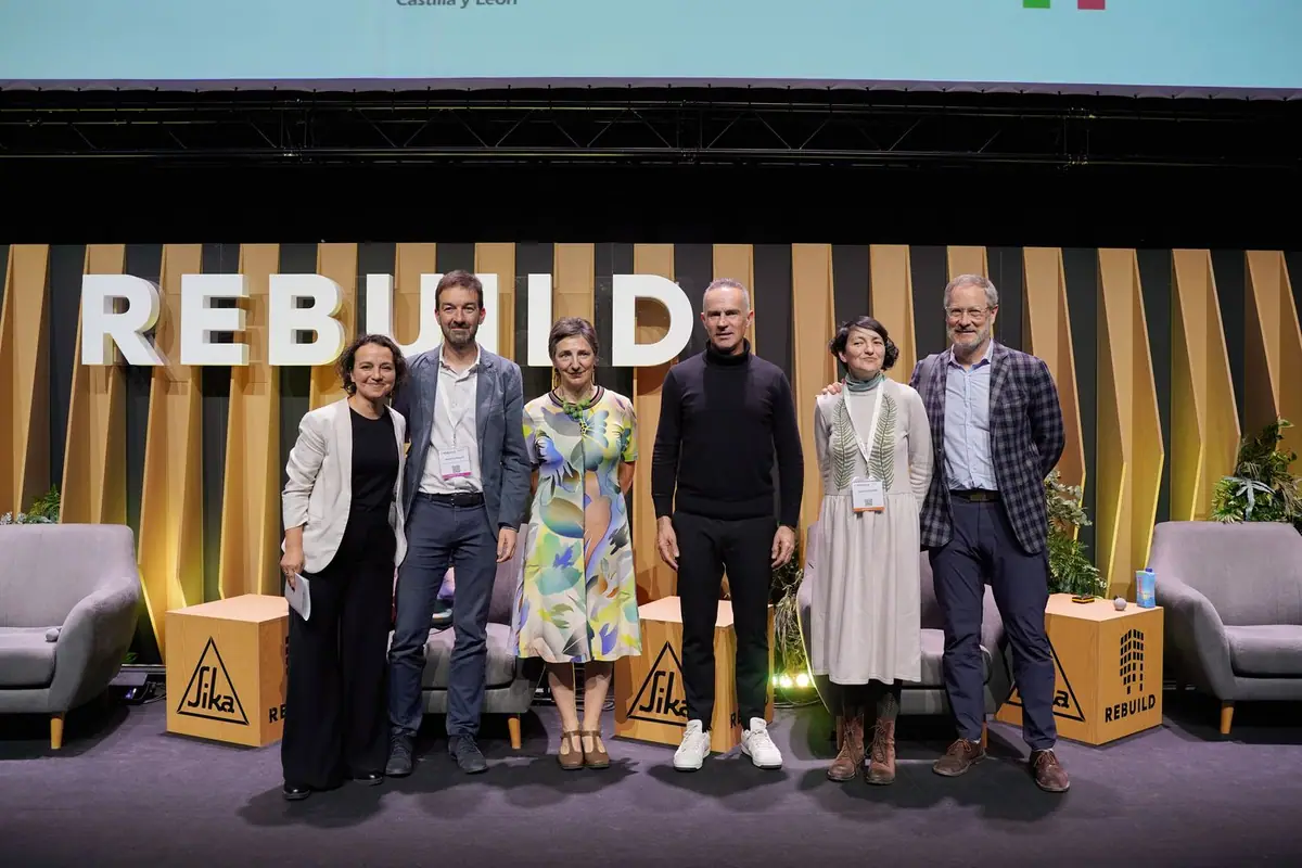 Los ponentes de la mesa redonda posan de pie en el escenario de REBUILD, con el logotipo de la feria al fondo