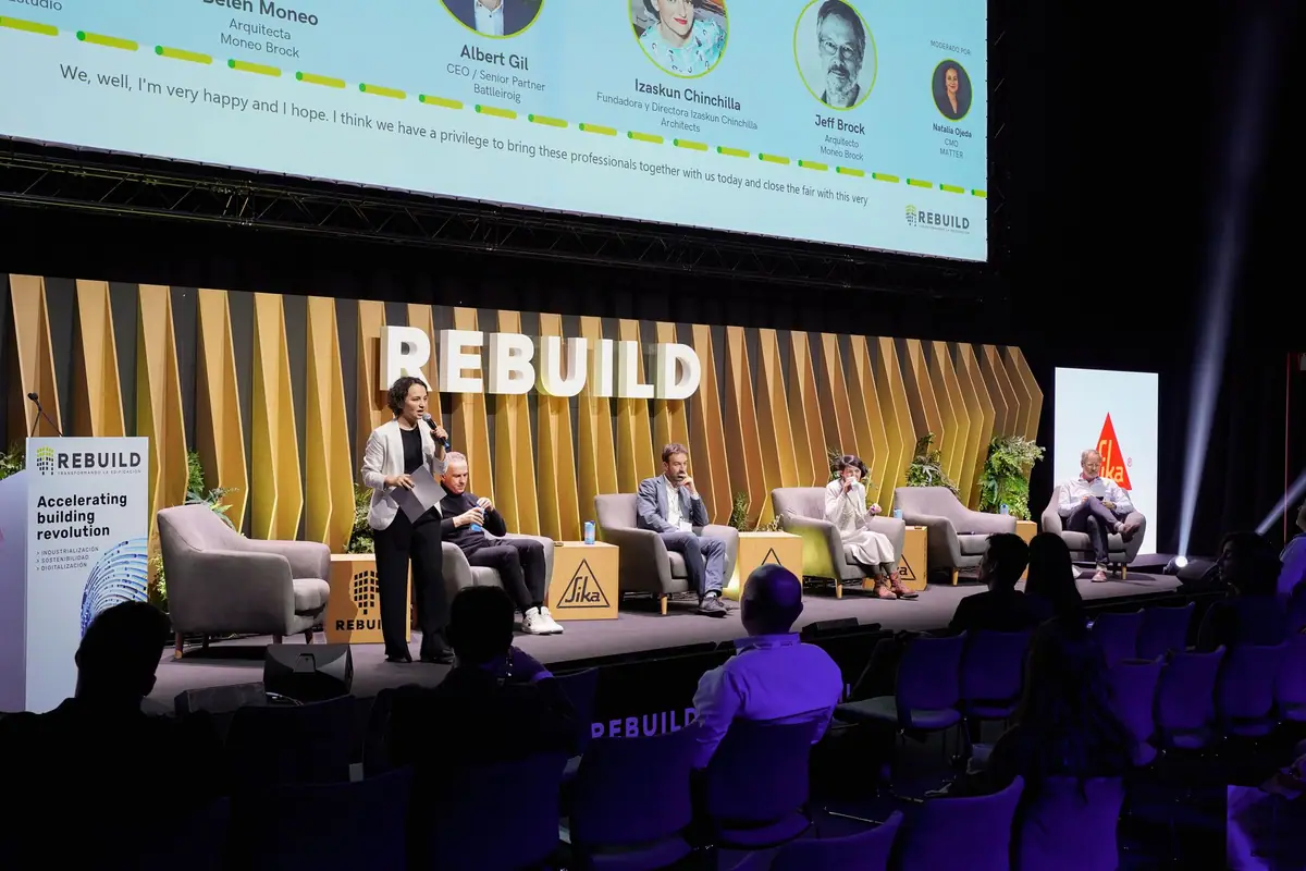 Vista del escenario durante la mesa redonda, con los ponentes sentados y una pantalla con sus nombres