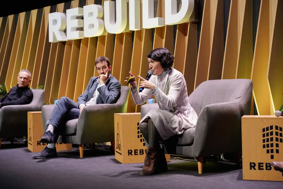 Tres ponentes sentados en el escenario; una de ellas interviene gesticulando