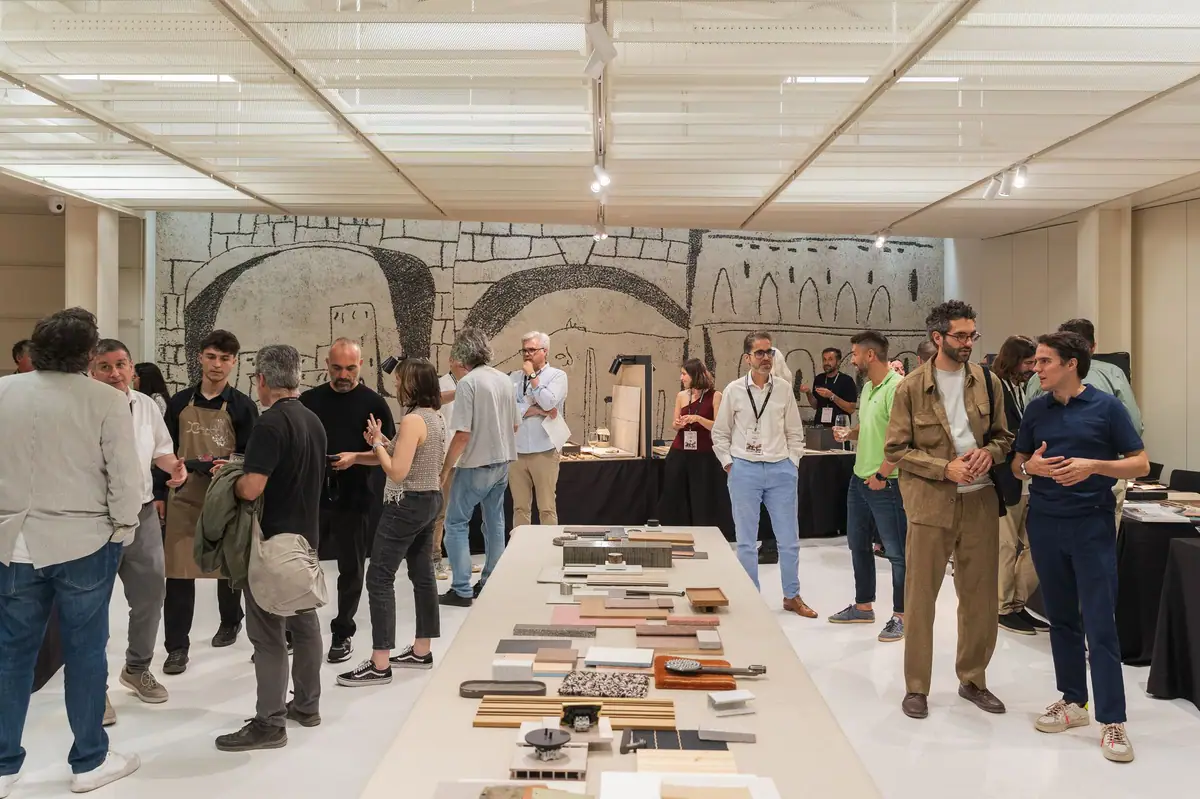 Profesionales conversando alrededor de una mesa de muestras de materiales junto a un mural esgrafiado de Picasso en el COAC.
