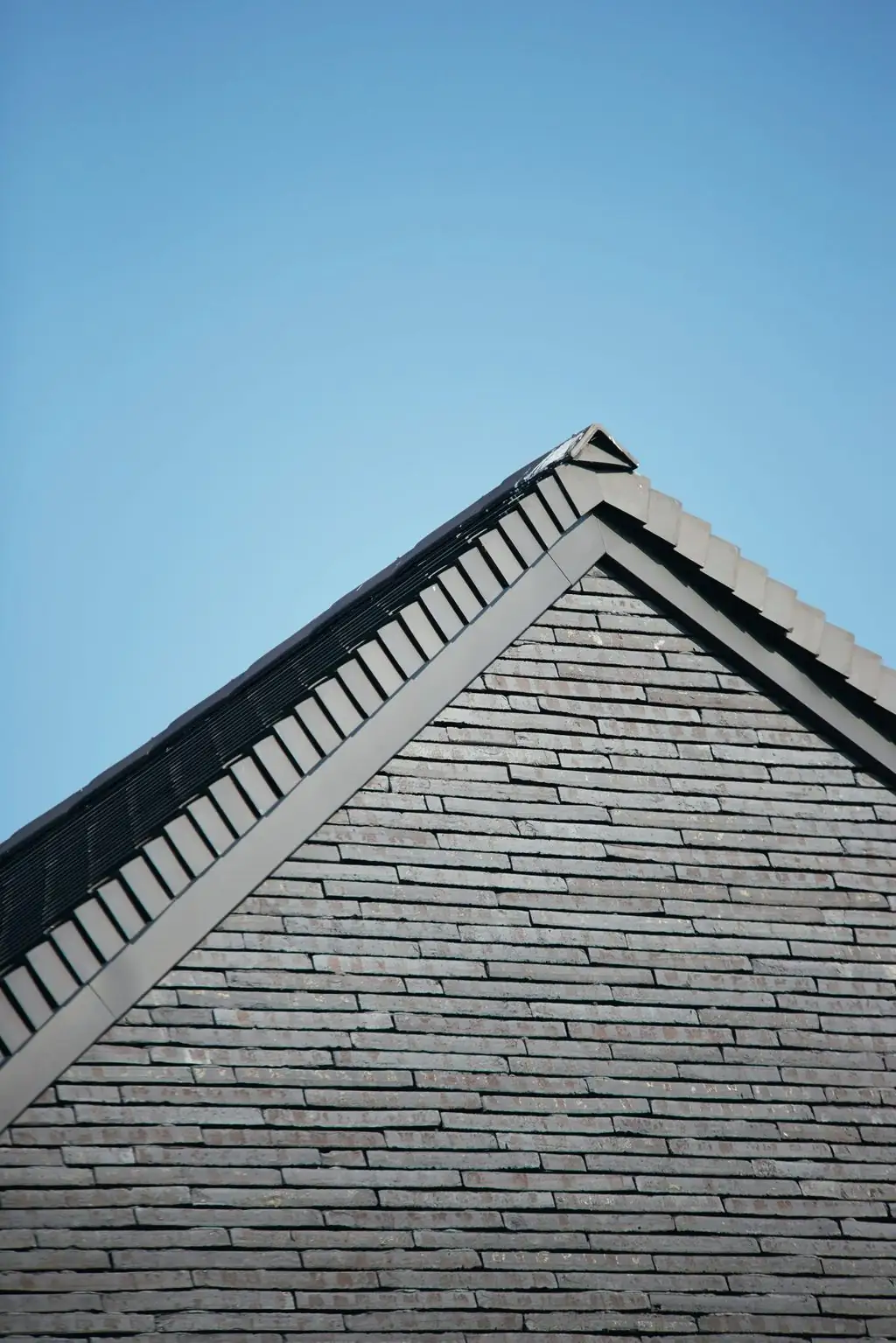 Hastial de una vivienda revestido con ladrillos largos y finos en gris oscuro bajo un cielo azul