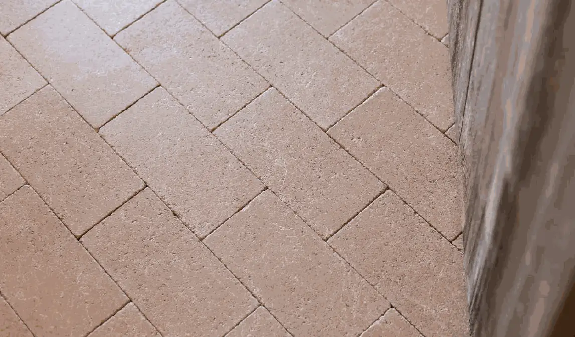 Pavimento de piezas rectangulares de piedra compactada en tono arena, colocadas a matajunta junto a un muro.