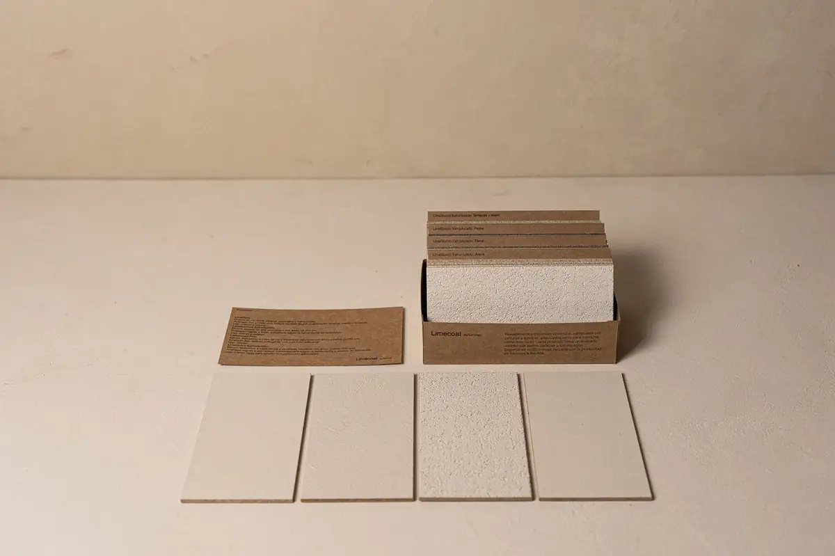 Caja de muestras de Limecoat abierta con cuatro placas de revestimiento de cal en tonos blancos delante.
