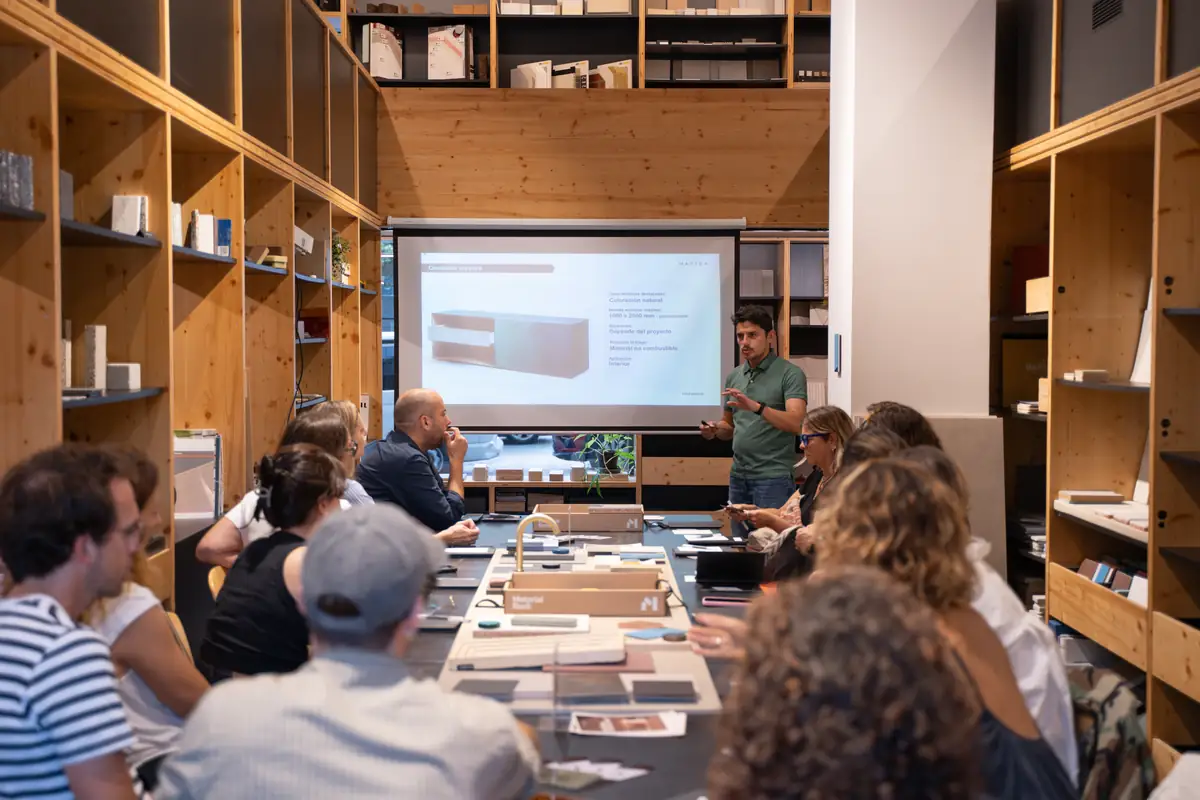 A Matter consultant presents a piece of furniture clad in patinated metal on a screen, in front of attendees seated at the Materials Library table.