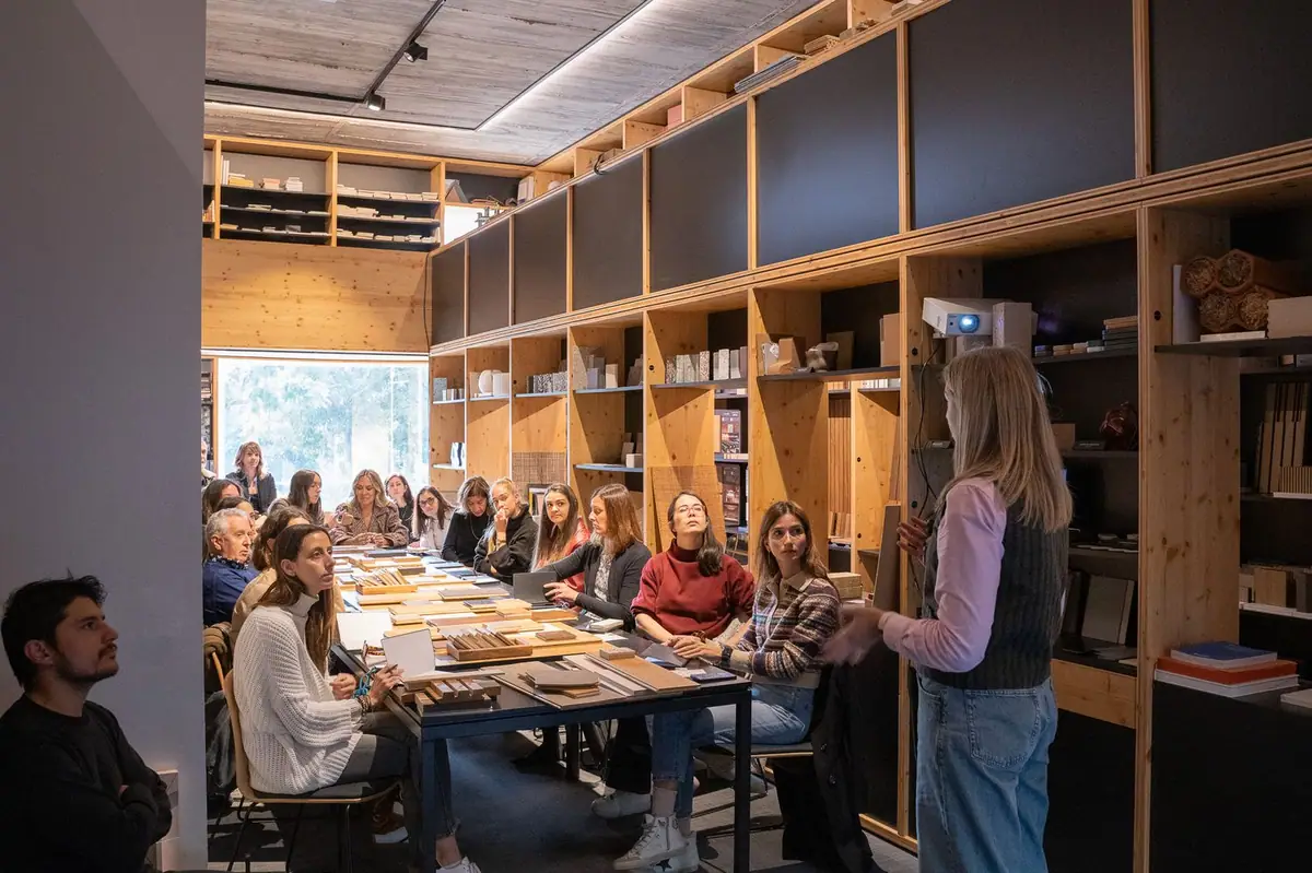 Andrea Pozzobon, standing, addresses the attendees seated around the sample table, in a room with wooden shelving.