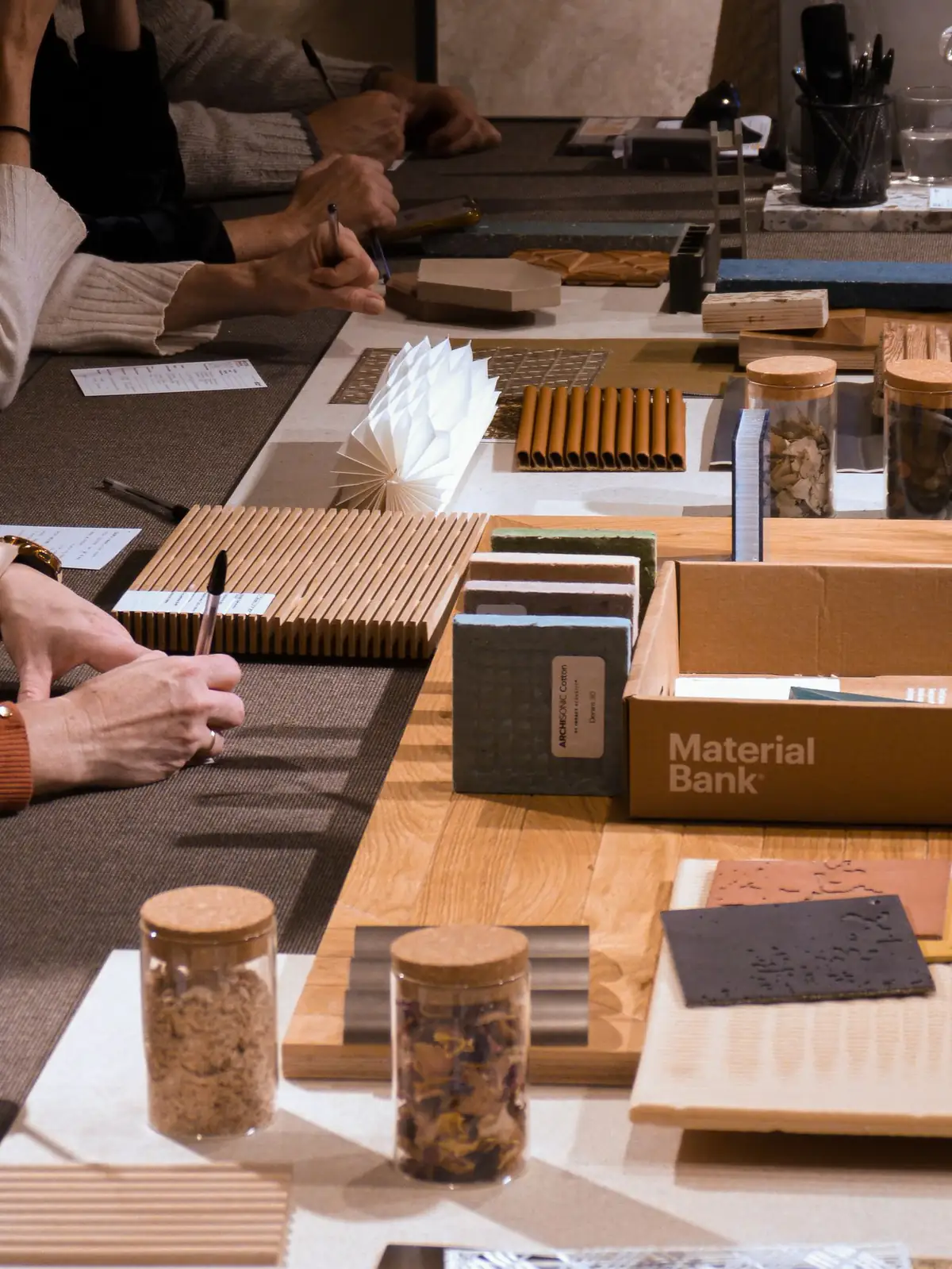 Detalle de la mesa con muestras de madera, botes de áridos y una caja de Material Bank.