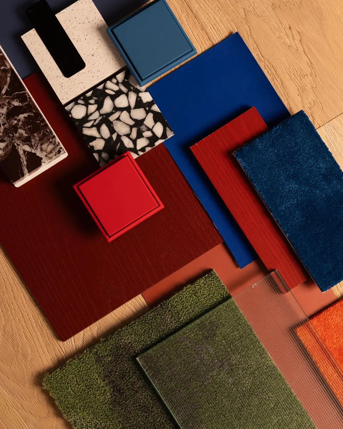 Composition of material samples in reds, blues and greens: carpets, fluted glass, terrazzo and stone on a wooden floor