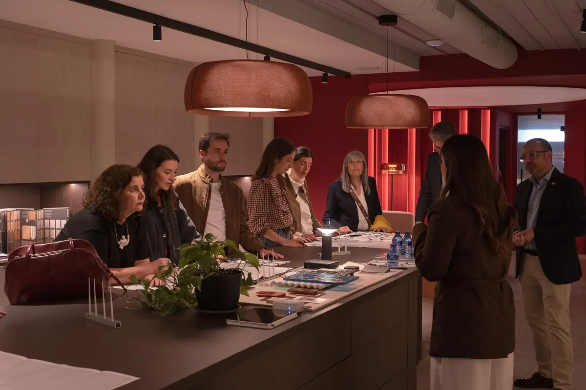 Asistentes alrededor de una mesa con muestras de materiales bajo lámparas de suspensión