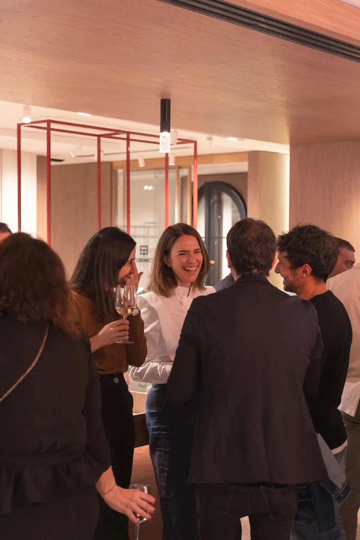 Asistentes conversando con copas de vino junto a una estructura metálica roja