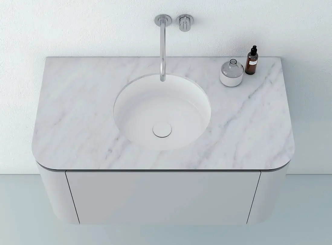 Vista superior de un mueble blanco de laterales curvos con encimera de mármol blanco veteado y lavabo redondo